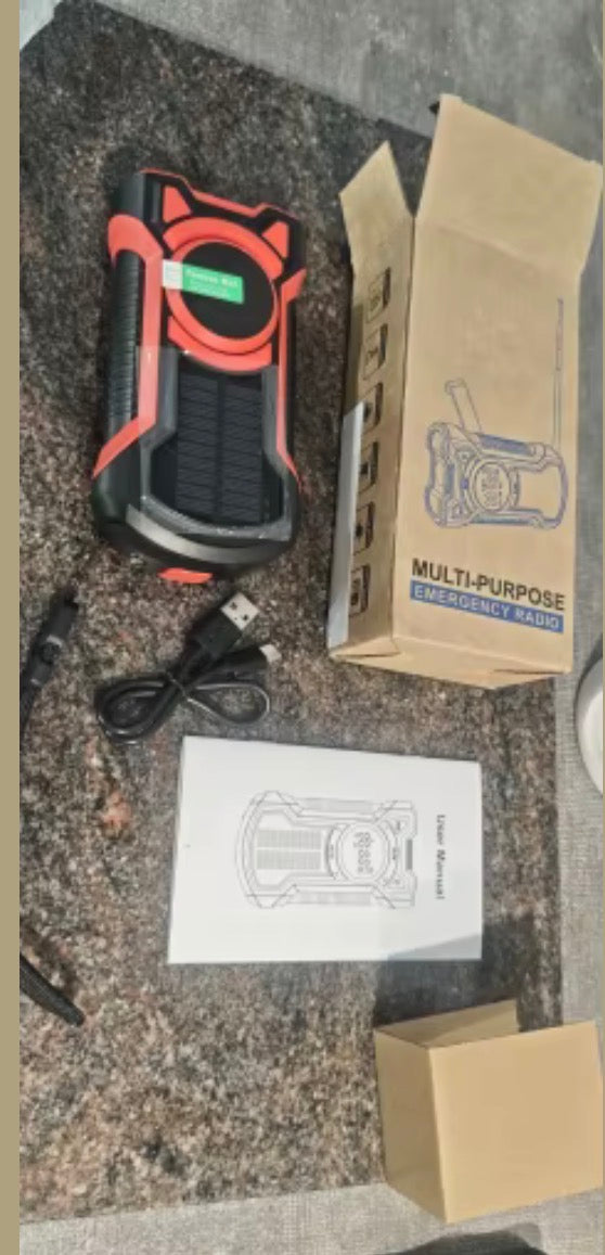 Multi-purpose emergency radio with solar panel, USB cable, user manual and packaging on table