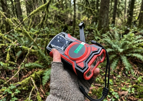 Hand holding emergency radio with solar panel and flashlight in a forest setting