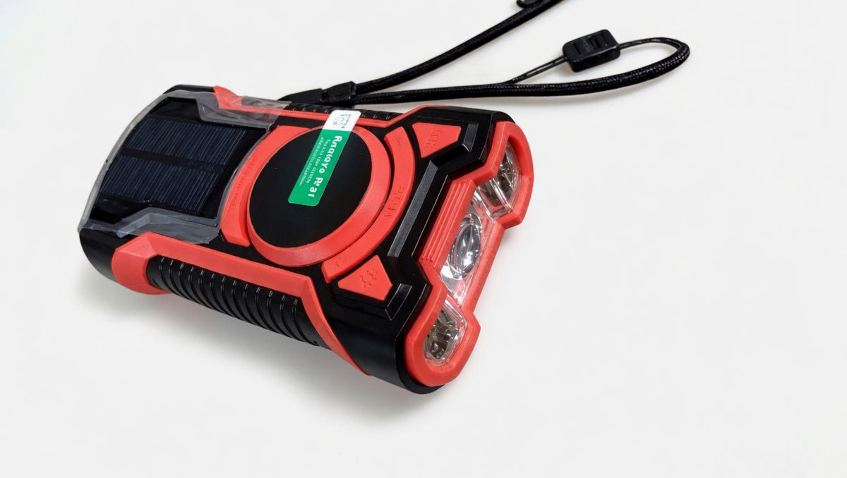 Red and black emergency solar radio with flashlight and hand strap on white background